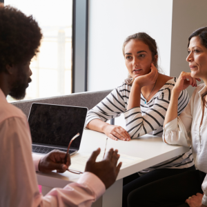 Black man with natural hair looking at laptop while talking to two women