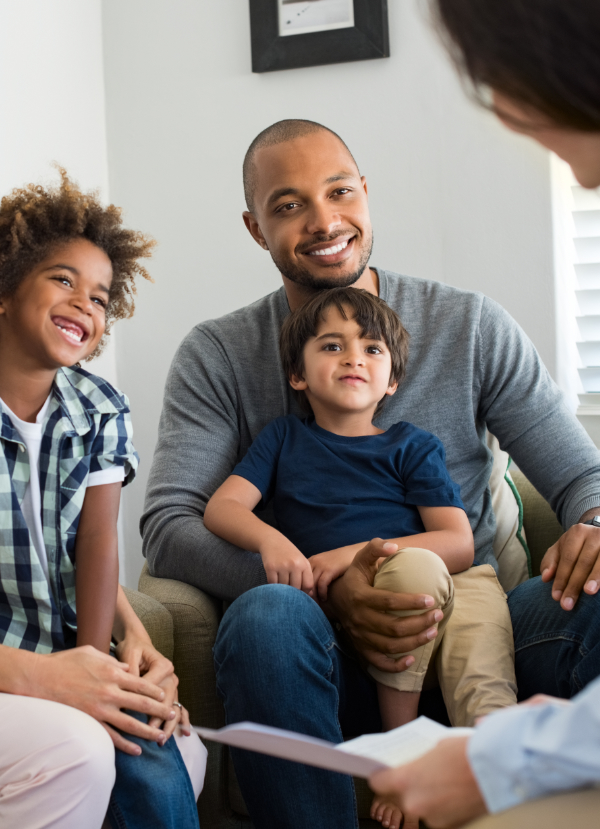 Happy young family sitting on couch and talking with family counselor. Smiling parents with adopted children discussing with counselor. Multiethnic family meeting a financial agent.