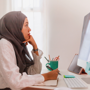 Woman of color wearing hijab, working at a computer on a desk