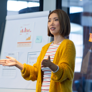 Asian woman standing in front of a whiteboard talking to people in the room