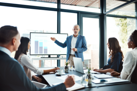 Middle-aged white man in professional clothes presenting a graph chart to a room of people