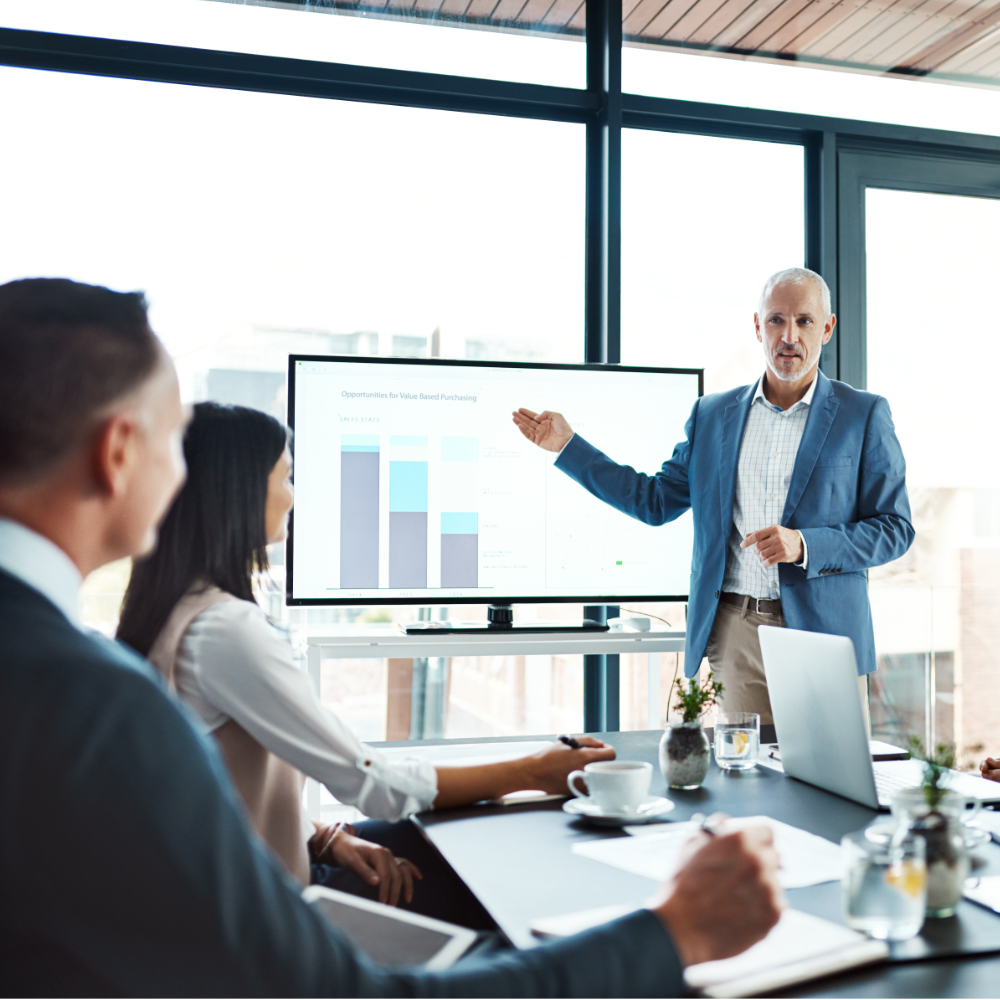 Middle-aged white man in professional clothes presenting a graph chart to a room of people